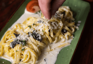 Hände die Käse auf Pasta treuen im Restaurant Wulfsmühle