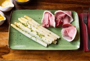 Teller auf Holztisch mti Spargel und Schinken im Restaurant Wulfsmühle