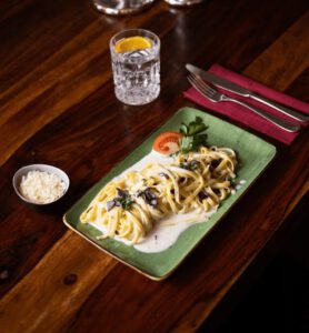 Lecker angerichteter Teller auf Holztisch mit Pasta dazu ein Getränk in einem edlen Glass im Restaurant Wulfsmühle