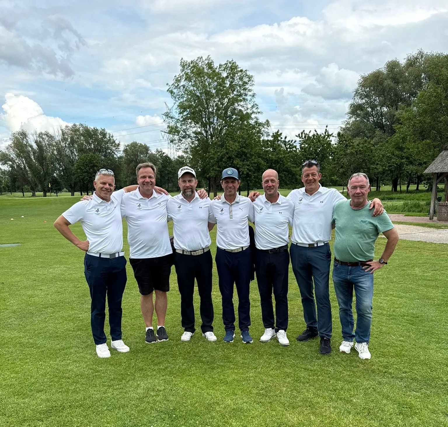 Sieben Männer posieren auf einem Golfplatz, sechs davon tragen weiße Team-Poloshirts